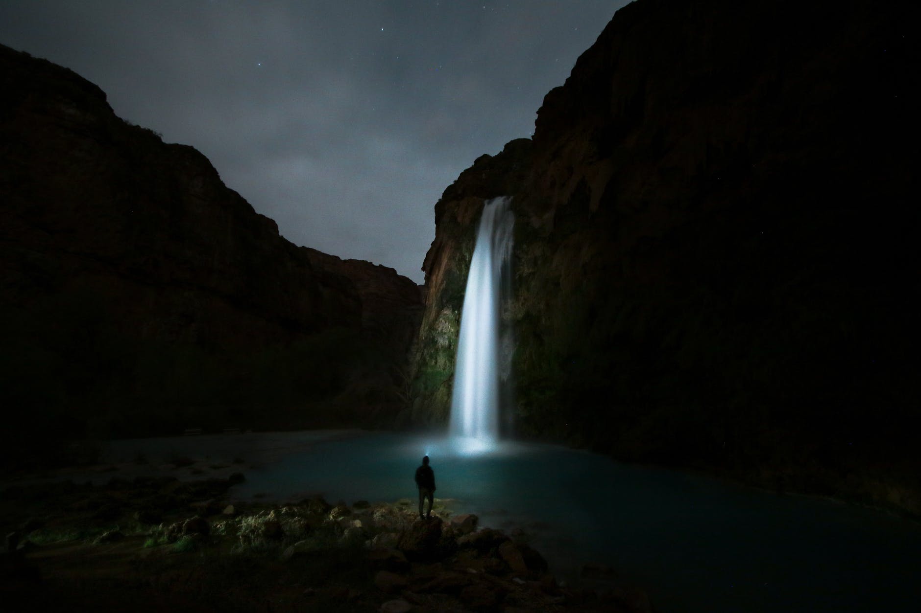 person standing beside waterfalls in dark lighting with torch