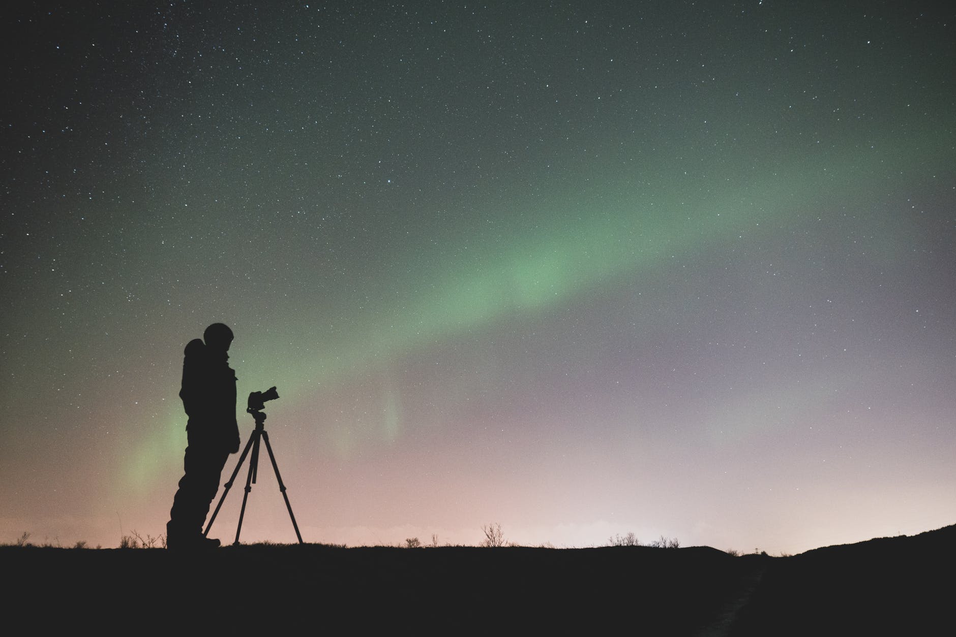 silhouette of person standing near a tripod for video shooting and photography under green sky with stars