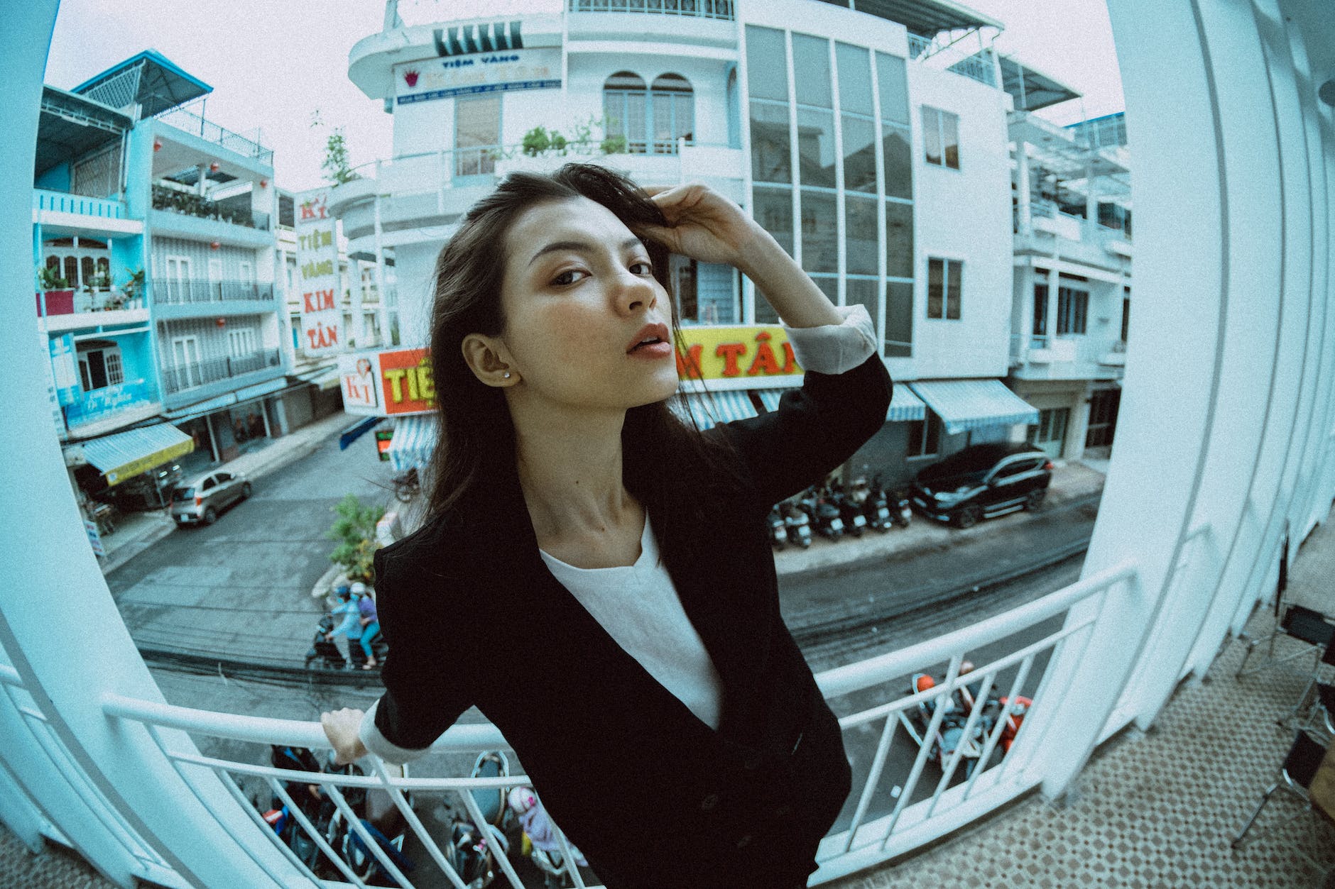 stylish asian woman on balcony against urban houses taken with fisheye lens